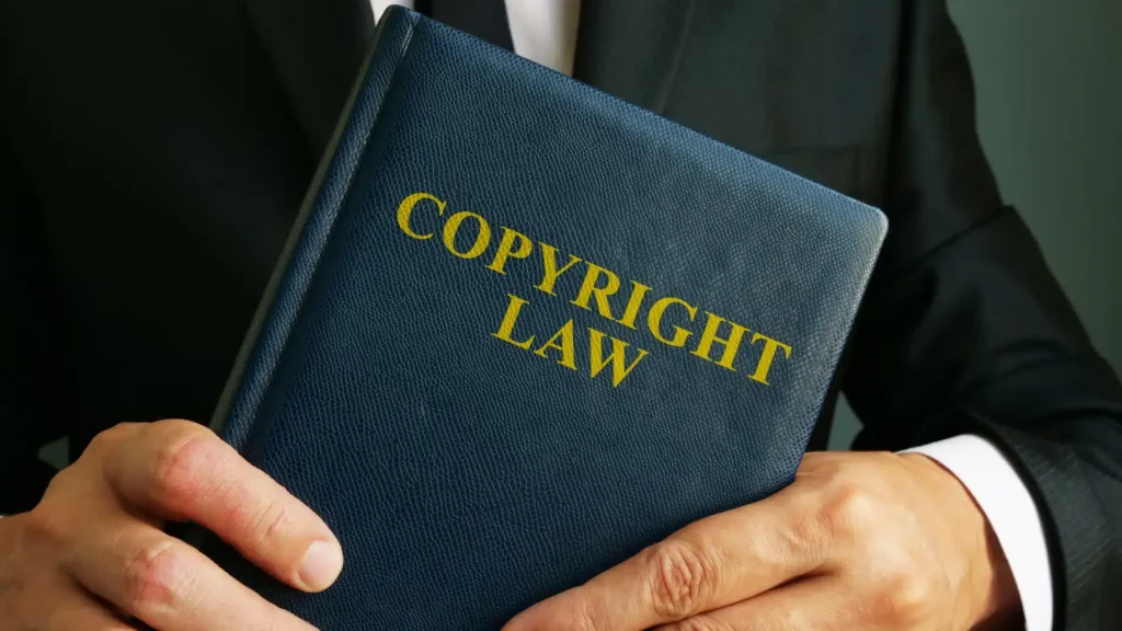 Person holding a blue book labeled “Copyright Law,” symbolizing intellectual property rights and legal protection for creators.