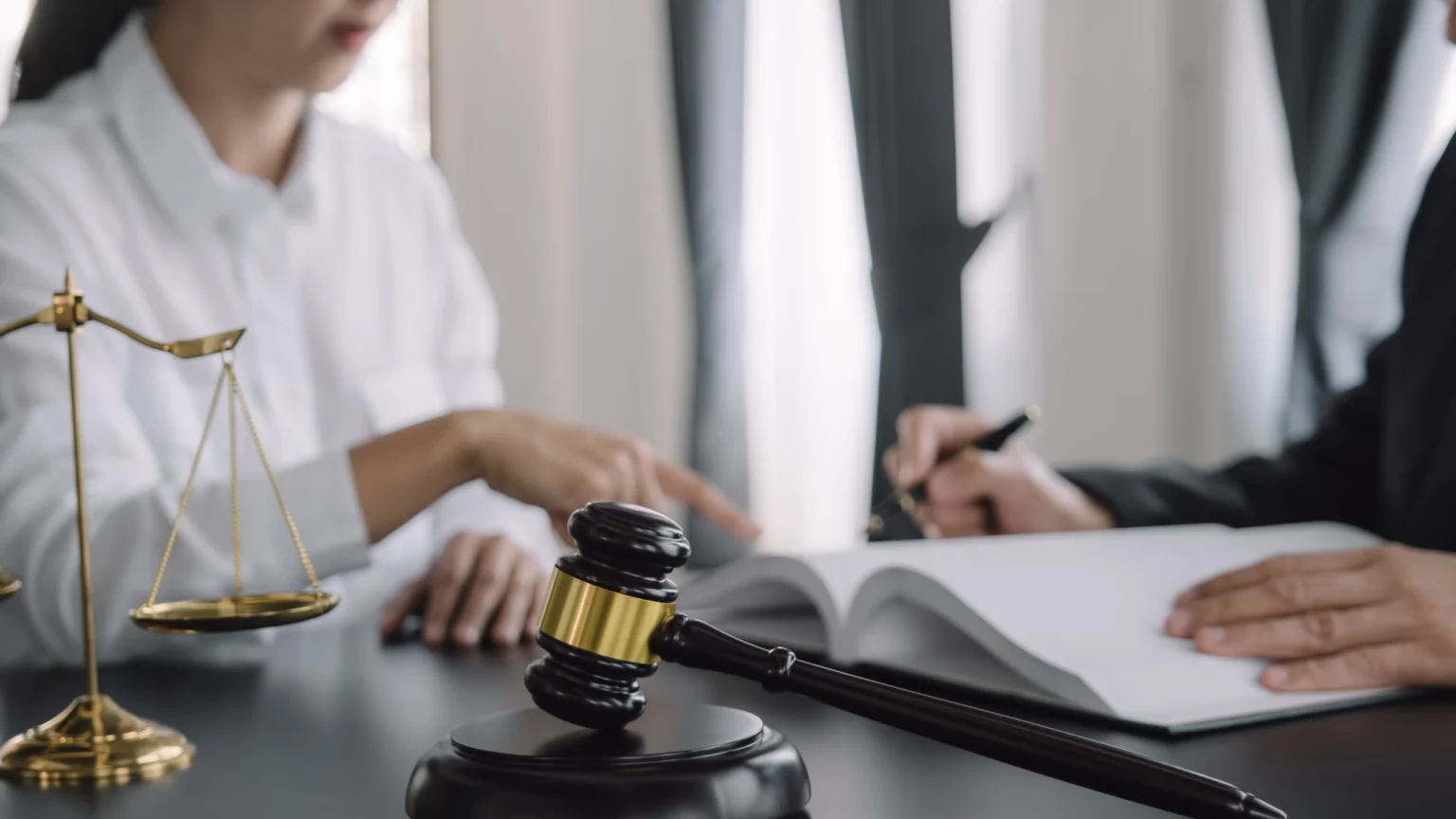 Lawyer writing or signing legal documents while holding a gavel, symbolizing contract approval or settlement.